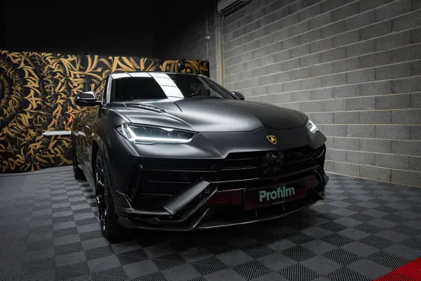 Mat siyah kaplamalı Lamborghini Urus Performansı, altın aksanlı sanat eserleriyle dolu bir duvara dayalı, kapalı bir zeminde sergileniyor..