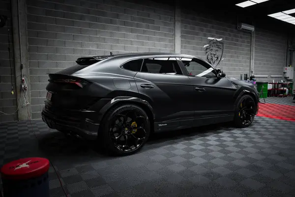 Siyah bir Lamborghini Urus Performante modern bir garajda beton duvarlar ve kareli zeminde stilize edilmiş bir boğa logosu ile park edilmiştir..