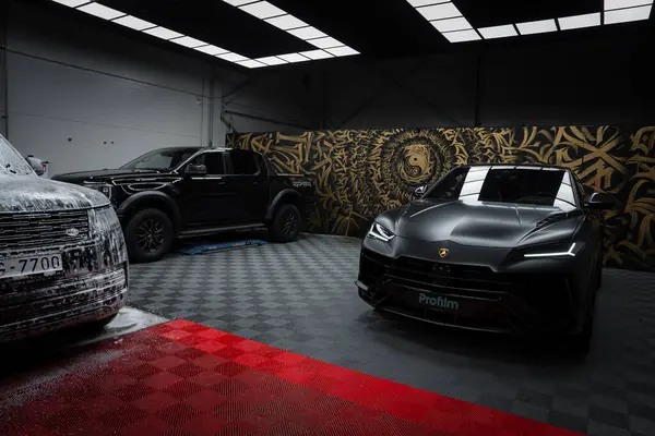 Gösterişli, siyah bir Lamborghini Urus Performante kapalı bir yerde kareli bir zeminde, arka planda parlak bir sergi salonunda bir aslan duvar resmi ile park edilir..