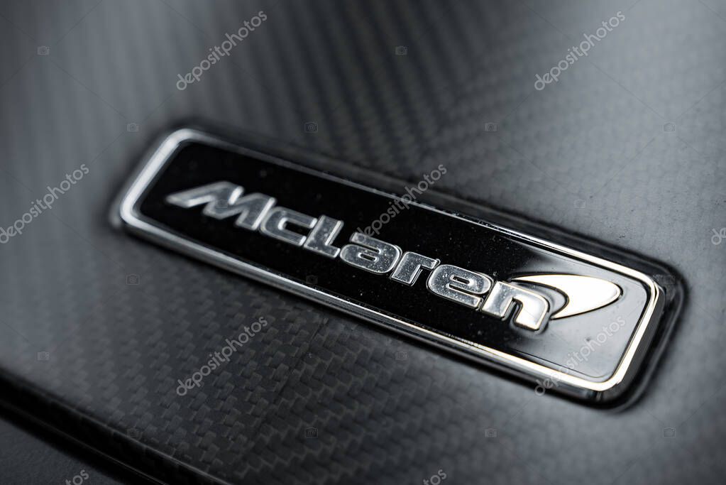 A detailed view of the McLaren emblem in silver on a black background, set against a sleek carbon fiber texture, highlighting luxury craftsmanship.
