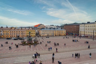 Finlandiya 'nın Helsinki kentindeki Senato Meydanı' nda neoklasik binalar, yeşil kubbeli Helsinki Katedrali ve hareketli bir kalabalığın ortasında Alexander II heykeli bulunur..