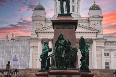 Helsinki Katedrali 'nin neoklasik mimarisi ve yeşil kubbeleri, önünde Alexander II heykeli olan canlı bir günbatımı gökyüzüne karşı duruyor..