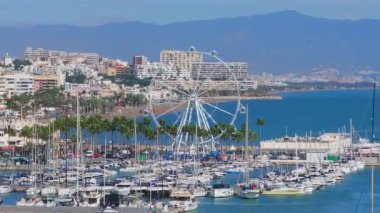 Benalmadena, İspanya 'nın havadan görünüşü, içinde tekneler, renkli binalar, dönme dolap ve ufukta uzak dağlar olan bir marinaya ev sahipliği yapıyor..