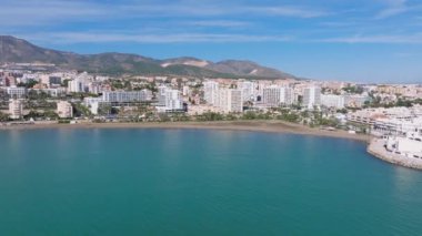 Benalmadena, İspanya 'nın havadan görünüşü, sahile yakın yüksek binalar, kumlu plaj, yeşil tepeler, ve güneşten keyif alan insanlarla dolu açık mavi gökyüzü..