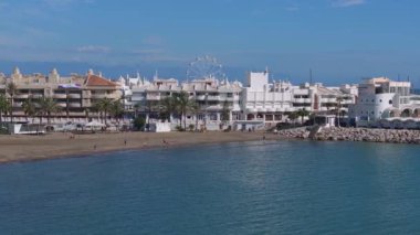 Benalmadena, İspanya 'nın havadan görünüşü, açık mavi gökyüzü altında, içi palmiye ağaçları, güneşlenenler ve modern yüksek binalarla dolu kumlu bir plaj..