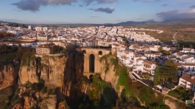 Ronda 'nın Puente Nuevo köprüsü El Tajo geçidini kapsar, kayalıklarda beyaz boyanmış binalar ve gün batımının ılık parıltısında yuvarlanan tepeler.