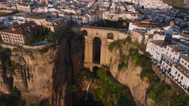 Ronda 'nın Puente Nuevo köprüsü, altın bir günbatımı parıltısının altında beyazlatılmış binalar ve uçurumlarla çevrili El Tajo geçidini kapsar..