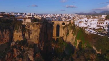 İspanya 'nın Ronda kentinin havadan görünüşü Puente Nuevo köprüsünü, beyazlatılmış binaları ve şehrin üzerinde altın bir parıltıyla gün batımında bir arenayı gösteriyor..