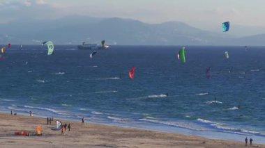Uçurtma sörfçüleri rüzgârlı Tarifa sahillerinde gezinirler. Palomas Adası deniz feneri ve Fas 'ın dağları Cebelitarık Boğazı boyunca görünür..