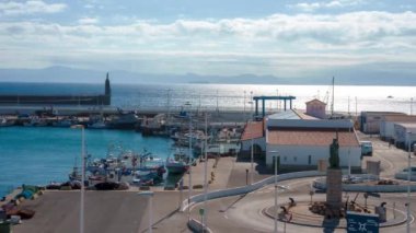Tarifa 'nın limanı balıkçı tekneleriyle dolup taşıyor. Kavşakta göze çarpan bir heykel ve boğazın karşısında Fas' ın olduğu Atlantik Okyanusu..