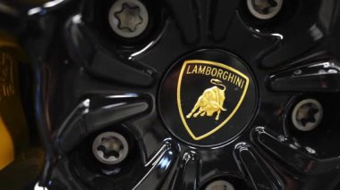 Lamborghini Urus tekerleğinin ayrıntılı görüntüsü, boğa logosu, parlak siyah bitiş ve sarı fren ayarları, lüks ve performans gösterimi.
