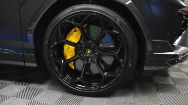 Lamborghini Urus 'un galeride detaylı görüntüsü, siyah alaşımlı tekerleklere ve fayanslı zemine karşı sarı fren kalibrelerine odaklanıyor..