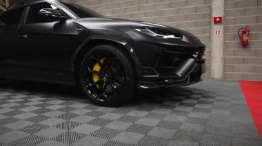 Video, Lamborghini Urus 'u bir sergi salonunda, tuğla duvarlara karşı mat siyah dış ve ayırt edici far tasarımı üzerine odaklanarak yakalıyor..