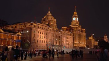 Şangay 'daki Bund kalabalıkla dolu ve gökyüzüne karşı ikonik saat kulesinin yer aldığı tarihi binalar aydınlatılıyor..