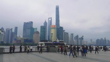 Şangay 'ın Bund' unun ikonik silueti, Şangay Kulesi ve Doğu İnci Kulesi 'nin görüntüsü, bulutlu bir gökyüzüne karşı kurulmuş ve canlı bir gezinti alanı..