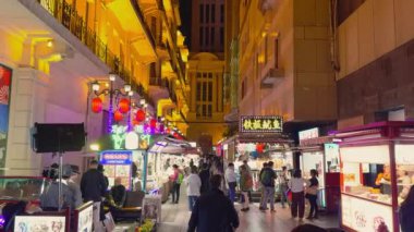 Geceleyin hareketli bir Şangay sokak pazarı, neon ışıkları ve kırmızı fenerlerle aydınlatılmış, çeşitli kalabalıklar ve modern ve geleneksel mimarinin karışımı..