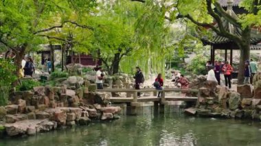 Ziyaretçiler Şangay 'daki Yu Gardens' ı keşfediyor, yemyeşil ve geleneksel Çin pavyonlarıyla çevrili bir göletin üzerindeki taş köprüyü geçiyorlar..