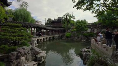 Şangay 'daki Yu Gardens' ta geleneksel pavyonlar, köprüler ve yemyeşil alanlar bulunuyor. Ziyaretçiler sakin bir göletin kenarındaki taş patikalarda gezinirler..
