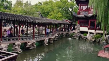 Ziyaretçiler Şangay 'daki Yu Gardens' ı keşfediyor. Karmaşık ahşap yapılar, eğimli çatılar, taş bir köprü, yemyeşil bir köprü ve canlı koi balığı bulunuyor..