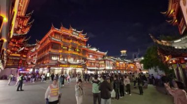 Şangay 'daki Yu Gardens geceleri aydınlanıyor. Geleneksel mimari ve arka planda modern ufuk çizgisi olan hareketli bir atmosfer sergiliyor..