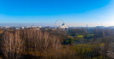 Riga 'nın eski kasaba ve şehir merkezinin hava manzarası. Victory Park' ta dönme dolap var. Televizyon kulesi açık mavi gökyüzüne ve çıplak ağaçlara karşı görünür..