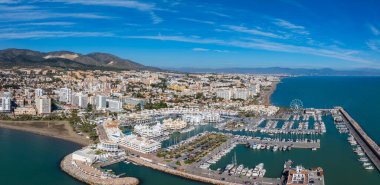 İspanya 'nın Benalmadena kentinin hava manzarasında yatları, kumlu plajları, dönme dolabı ve kayan tepelere karşı beyaz binaları olan canlı bir marina var..