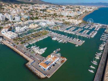 Görüntü, İspanya 'nın Benalmadena kentinin canlı bir yat, dönme dolap ve modern ve geleneksel mimarinin karışımından oluşan bir marinasını görüntülüyor..