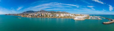 İspanya 'nın Benalmadena kentinin havadan görünüşü, açık mavi gökyüzü altında tekneleri, yüksek binaları ve Sierra de Mijas dağları olan bir marinaya ev sahipliği yapıyor..