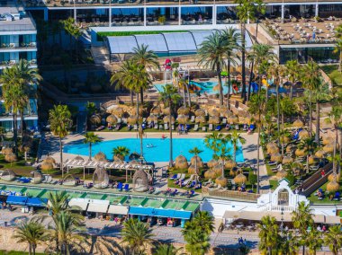 İspanya, Benalmadena 'da canlı bir havuz manzarası, palmiye ağaçları, dinlenme yerleri ve su oyun alanı. Resort binaları arka planda görünür..