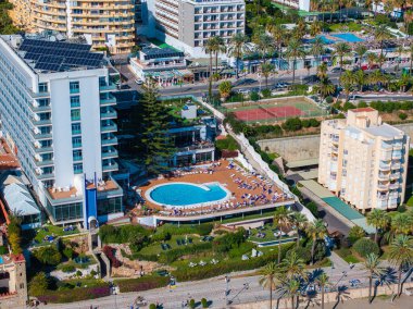 İspanya 'da bir Benalmadena tatil köyünün havuz manzarası, otelin çatısında güneş panelleri, tenis kortları ve palmiye ağaçlı yemyeşil bahçeler.