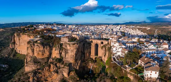 Ronda, İspanya gün batımında Puente Nuevo köprüsünün bulunduğu derin bir vadi, beyazlatılmış binalar ve dramatik bir uçurum kenarı manzarası görülür..