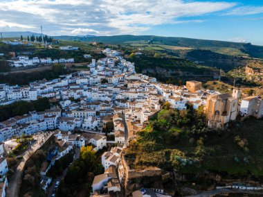 Setenil de las Bodegas, kayaların altında beyazlatılmış binalar, dolambaçlı sokaklar ve yeşil tepelerle çevrili bir tepede büyük bir kilise barındırır..