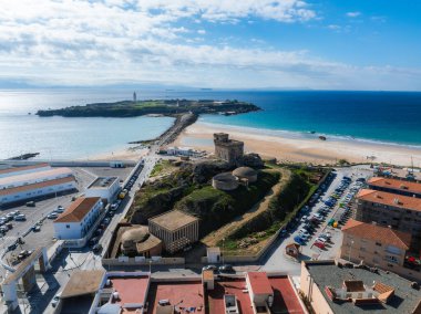 Tarifa 'nın kıyı manzarası Guzman el Bueno Kalesi, kumlu plajlar, uçurtma sörfçüleri ve yakınlarındaki kasaba binaları ile uzak bir deniz feneri içerir..