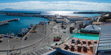 İspanya, Tarifa 'nın havadan görünüşü, tekneler, uzak bir deniz feneri ve açık, güneşli gökyüzünün altında havuzu olan bir çatı terası ile hareketli bir limanı gösteriyor..
