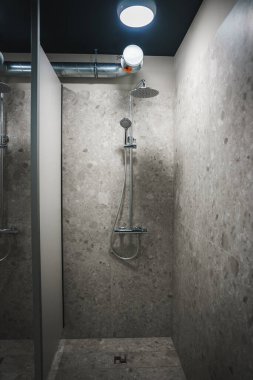 Gösterişli bir duş kabininde bir spor veya eğlence kompleksi içinde yer alan sağanak yağmur başlığı, açık gri taş fayanslar ve endüstriyel elementler yer alıyor..