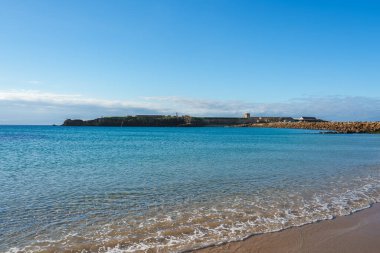 İspanya 'nın Tarifa kentinde sakin bir plajda Atlantik Okyanusu ve Castillo de Santa Catalina bulunur. Dağınık bulutlu açık gökyüzü huzurlu ortamı güçlendirir..