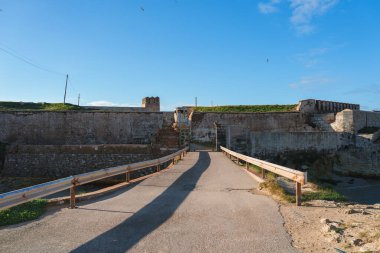 İspanya 'nın Tarifa kentindeki tarihi bir kalede yıpranmış taş duvarlar ve merkezi bir kule bulunuyor. Tahta parmaklıklı dar bir yol, temiz bir gökyüzünün altındaki girişe çıkar..