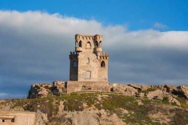 Torre de Guadalmesi, İspanya 'nın Tarifa kenti yakınlarındaki kayalık bir tepenin üzerinde duruyor. Parçalı bulutlu bir gökyüzü ve silindir şeklindeki sıcak günbatımı parlaklığıyla..