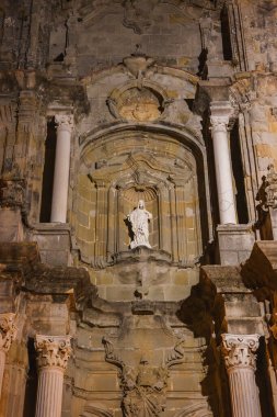 A detailed view of a historic stone facade in Tarifa, Spain, featuring a statue in an ornate niche, Corinthian columns, and intricate carvings at night. clipart