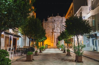 İspanya 'nın Tarifa kentindeki dar bir cadde gece aydınlanır. Saksı bitkileriyle doludur. Karmaşık oymaları ve büyük bir cephesi olan tarihi bir taş binaya götürür..