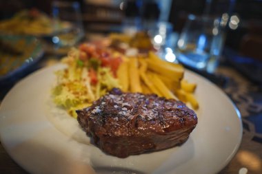 Izgara bifteğe yakın plan, sert tuzla süslenmiş, altın sarısı patates kızartması ve taze salata ile servis edilmiş, bir Tarifa, İspanya restoranında..