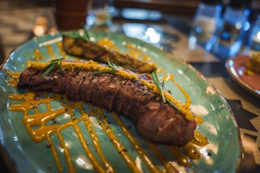 İspanya, Tarifa 'da bulanık bir masa ve cam parçasına karşı hazırlanmış turkuaz bir tabakta otlar ve sosla süslenmiş dilimlenmiş et tabağı..