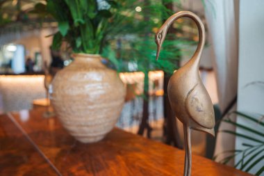 Parlatılmış ahşap bir masa dekoratif pirinç vinç heykeli içerir. Arka planda, yemyeşil yapraklı seramik bir vazo zengin ayarı artırır.