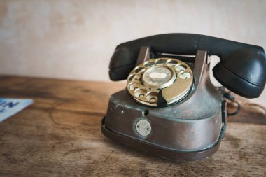 Eskimiş metalik kaplamalı klasik bir çevirmeli telefon, Marakeş temalı bir otelin sade dokulu duvarına dayalı, ahşap bir yüzeyde bulunur..