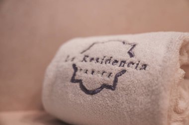 A plush towel with 'La Residencia' and 'Paris' embroidery, framed by a decorative border, set against a neutral background in a boutique hotel setting. clipart