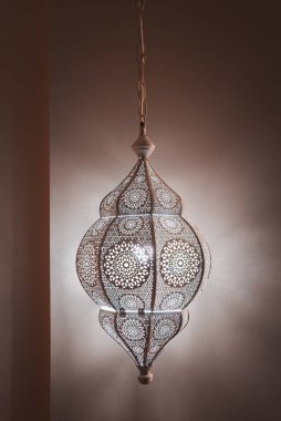 Detaylı metal işlemeli ve geometrik desenli bir Fas feneri duvarlara gölge düşürüyor ve Marakeş butik bir otelde sıcak bir atmosfer yaratıyor..