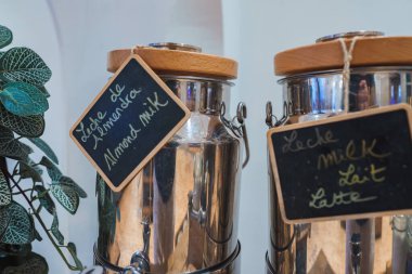 Badem sütü ve süt için ahşap kapaklı ve karatahta etiketli iki metal şeker kutusu, yemyeşil bitkilerle dolu lüks bir ortamda ayarlanmış..