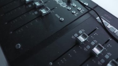 Ses karıştırma konsolunun faders ve kontrol düğmeleri detaylı bir görünümü, loş aydınlatılmış bir stüdyoda müzik üretiminin teknik yönlerini vurguluyor.