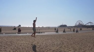 Los Angeles 'taki Venice Plajı yürüyen ve bisiklet süren insanlarla dolu. İkonik Santa Monica İskelesi, dönme dolabı ile, arka planda görünür..