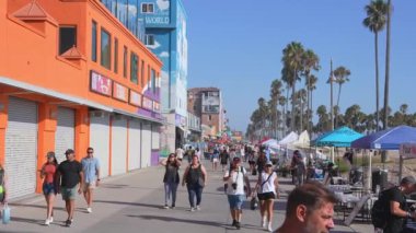 İnsanlar Venedik Plajı, Los Angeles 'ta güneşli bir günün tadını çıkarıyorlar. Renkli binalar, palmiye ağaçları, sokak satıcıları ve Aşk Duvarı duvar resmi canlı bir atmosfer yaratıyor..